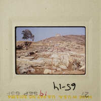 Ruins on hillside with vegetation and sky.