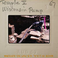 An old water pump with a motor on top, surrounded by rocks and debris.