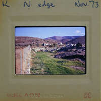 A photograph of a rural landscape with mountains, greenery, and a fence.