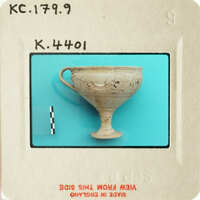 Ancient Greek cup with handle and face design, photographed on blue background.