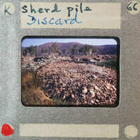 A pile of discarded items, possibly from a demolition site or construction waste, with mountains and trees in the background.