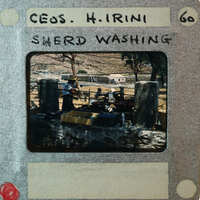 A vintage photo of a woman washing clothes by a river, with an old-fashioned appearance and handwritten label.