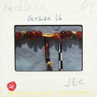 A red and gold necklace displayed on a white stand with a label.