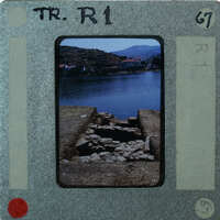 A vintage film strip with a photograph of a rural landscape featuring water and mountains.