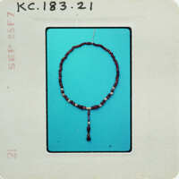 A small, circular rosary bead necklace with a crucifix pendant on a blue background.