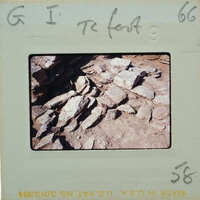 A photograph of a stone wall with dirt and rocks on the ground, displayed on a film strip.