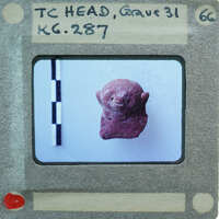 A small red figurine on a white surface with a ruler and labels around it.