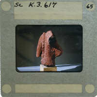 A photograph of a clay figurine torso, displayed on a stand.