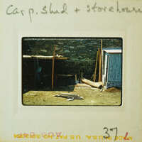 Old photograph of a dilapidated shed and storehouse with wooden structure, stone walls, and metal roof.