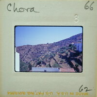 Old photograph of a mountainous village with white houses and greenery, framed by an aged paper border.