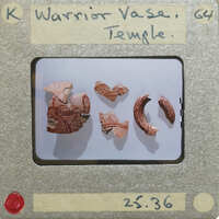 Unassembled fragments of vase with lines and warrior motif in red paint.